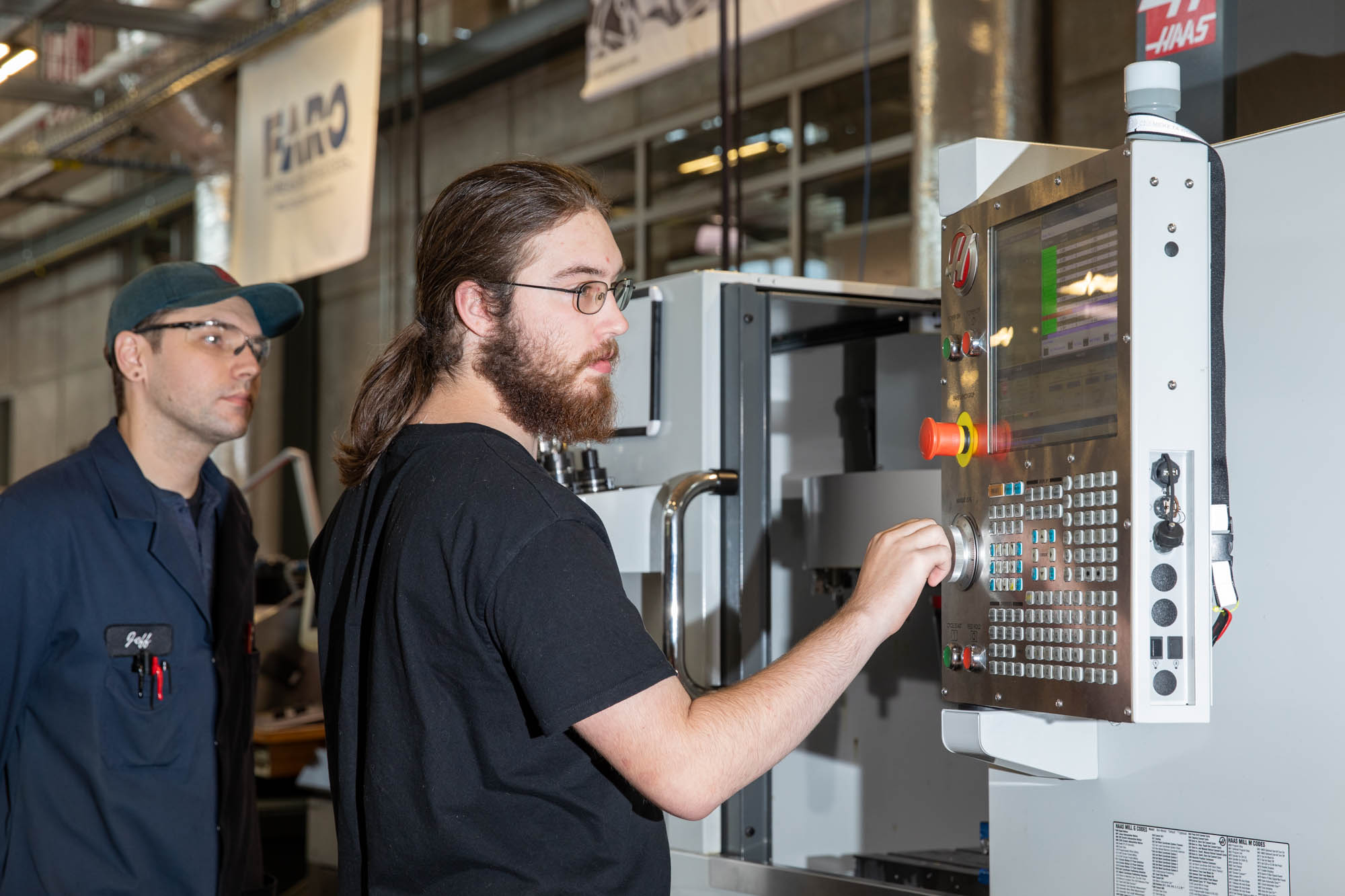A student works at the controls of a CNC machine as a instructor supervises.