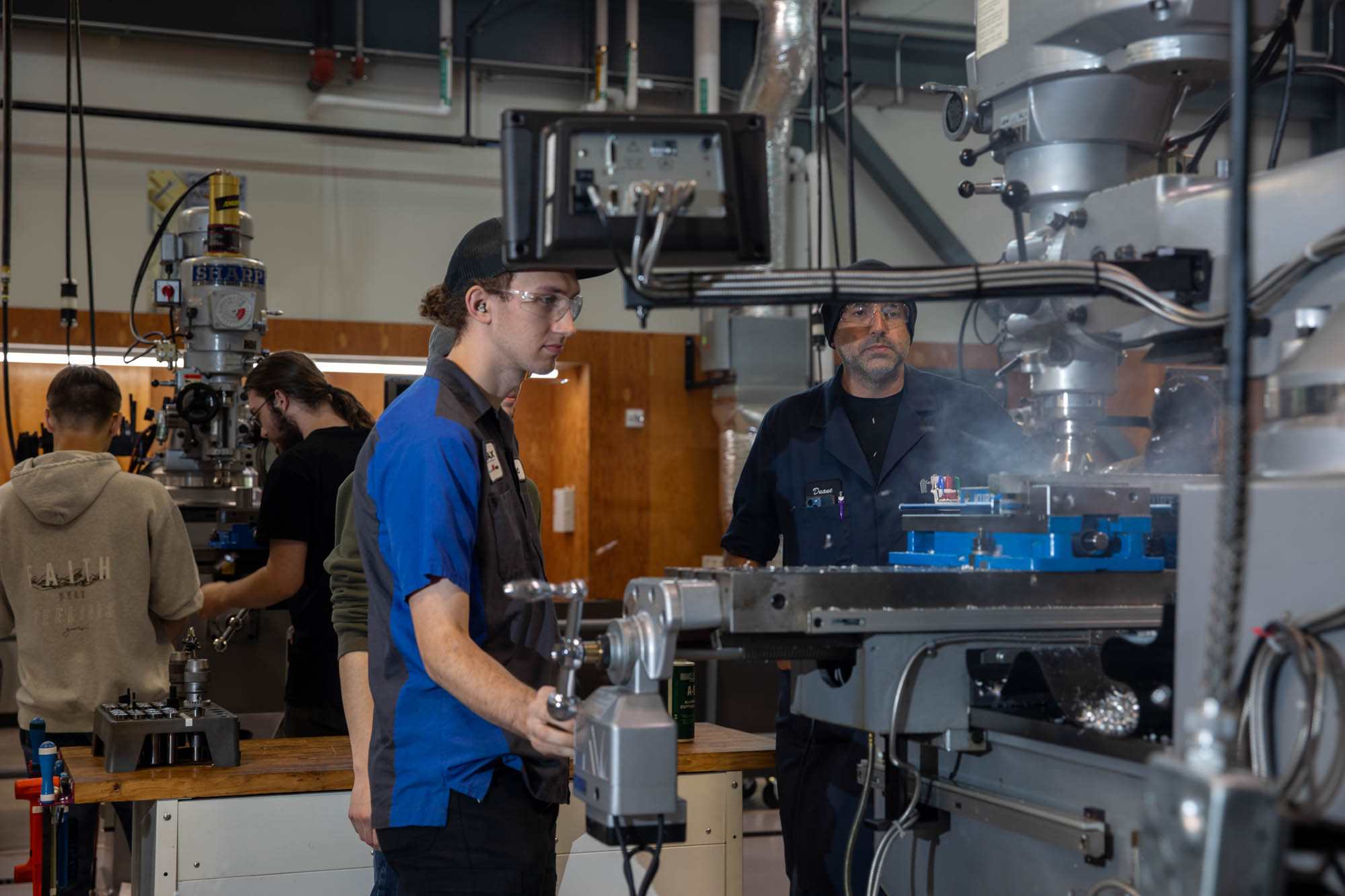 A student works in the machining lab as a faculty member supervises.